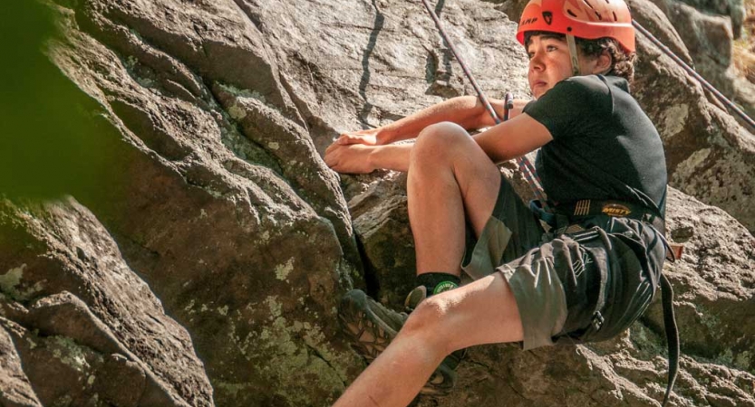 A person wearing safety gear is secured by ropes as they rock climb. 